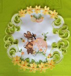 Wielkanocna serwetka o średnicy 30 cm w kolorze białym z wyhaftowanym zajączkiem malującym pisankę